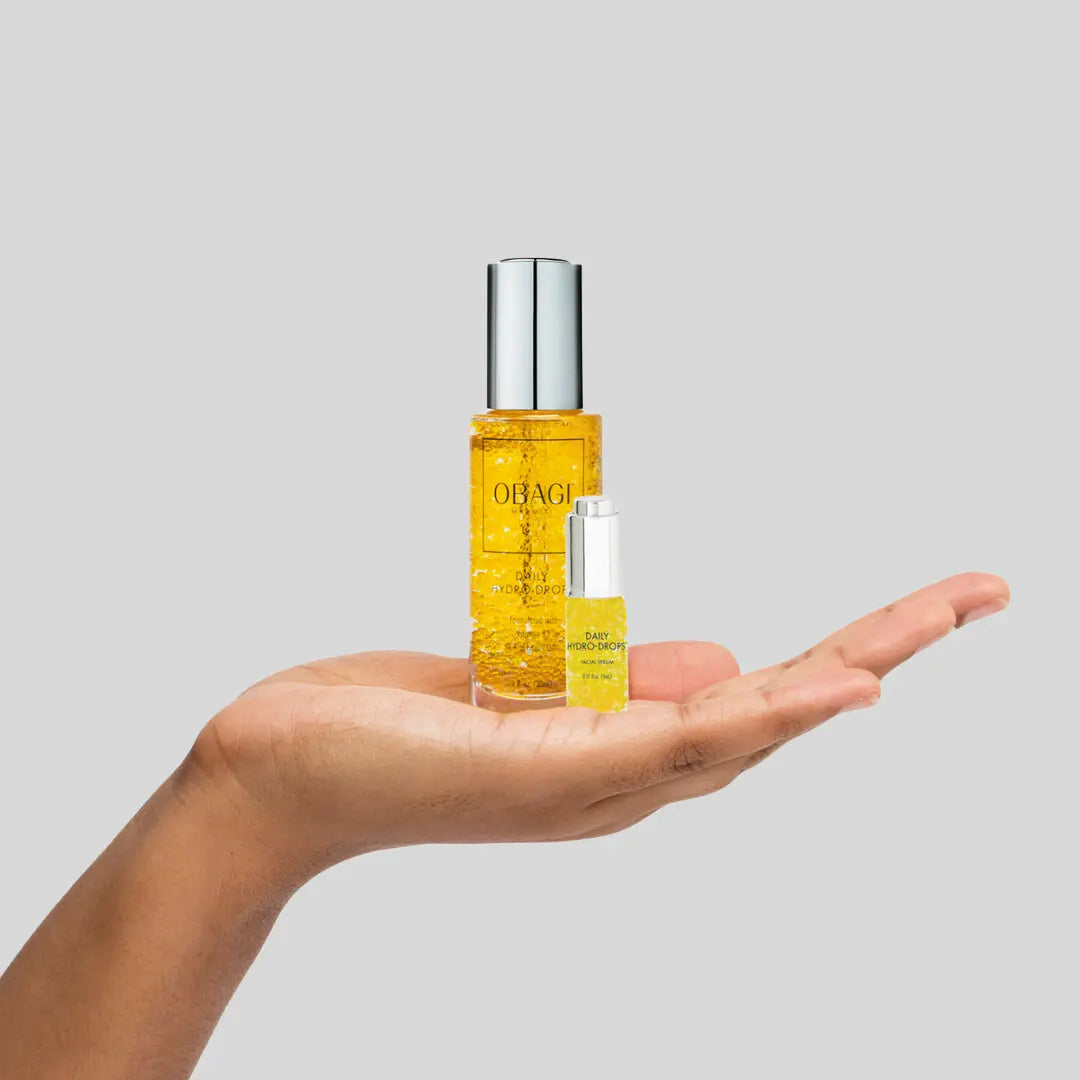 Hand holding two bottles of Obagi skincare product against a gray background