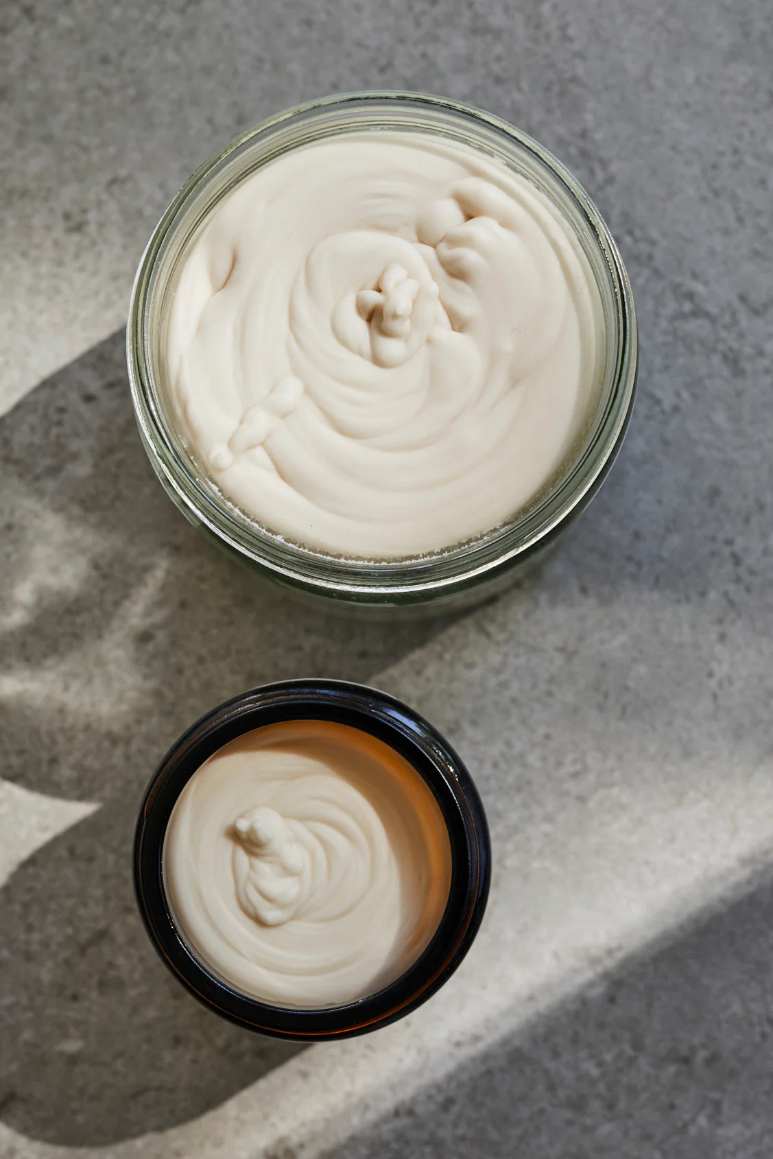 Two containers of white cream on a gray surface