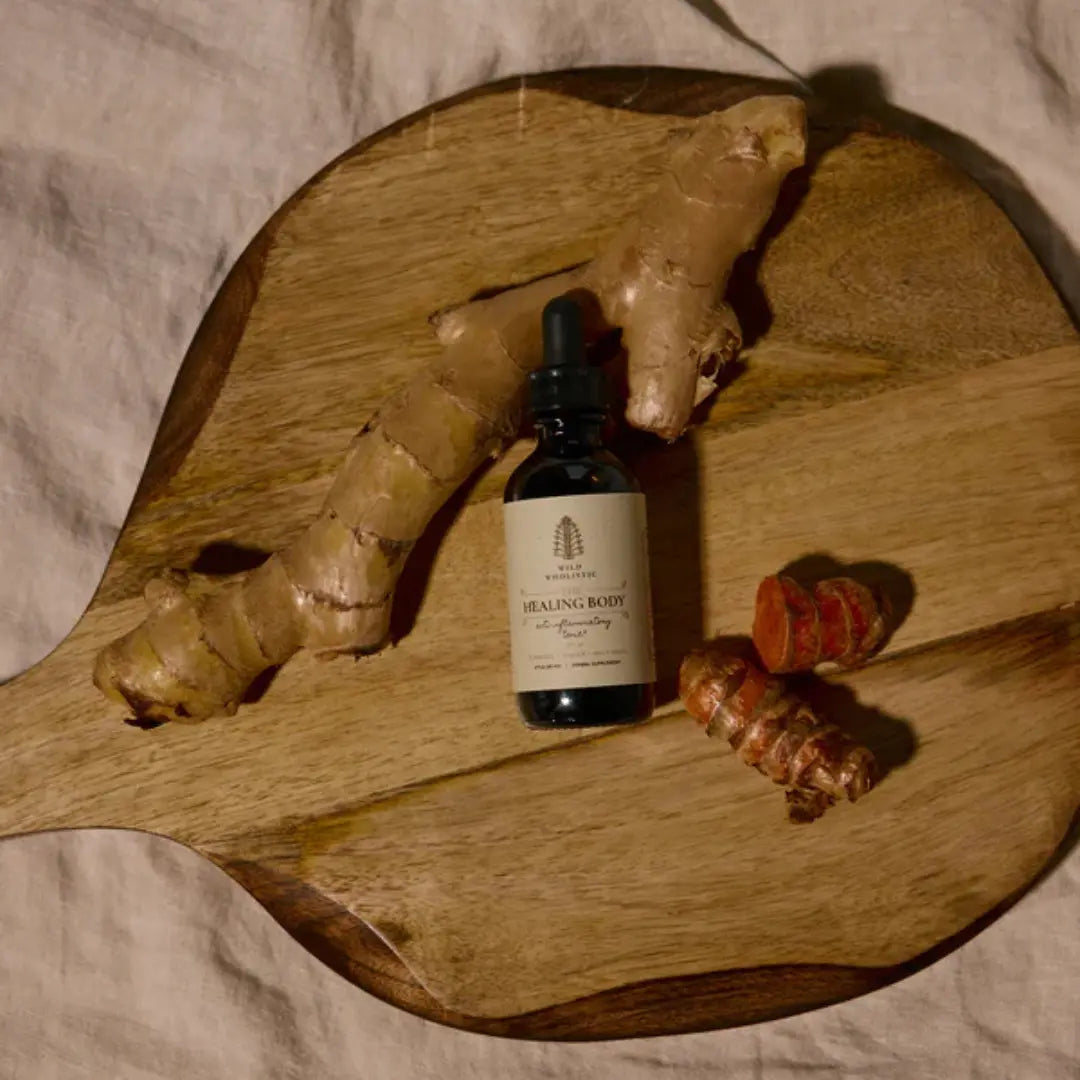 Bottle of 'Healing Body' serum on a wooden board with ginger root and turmeric.