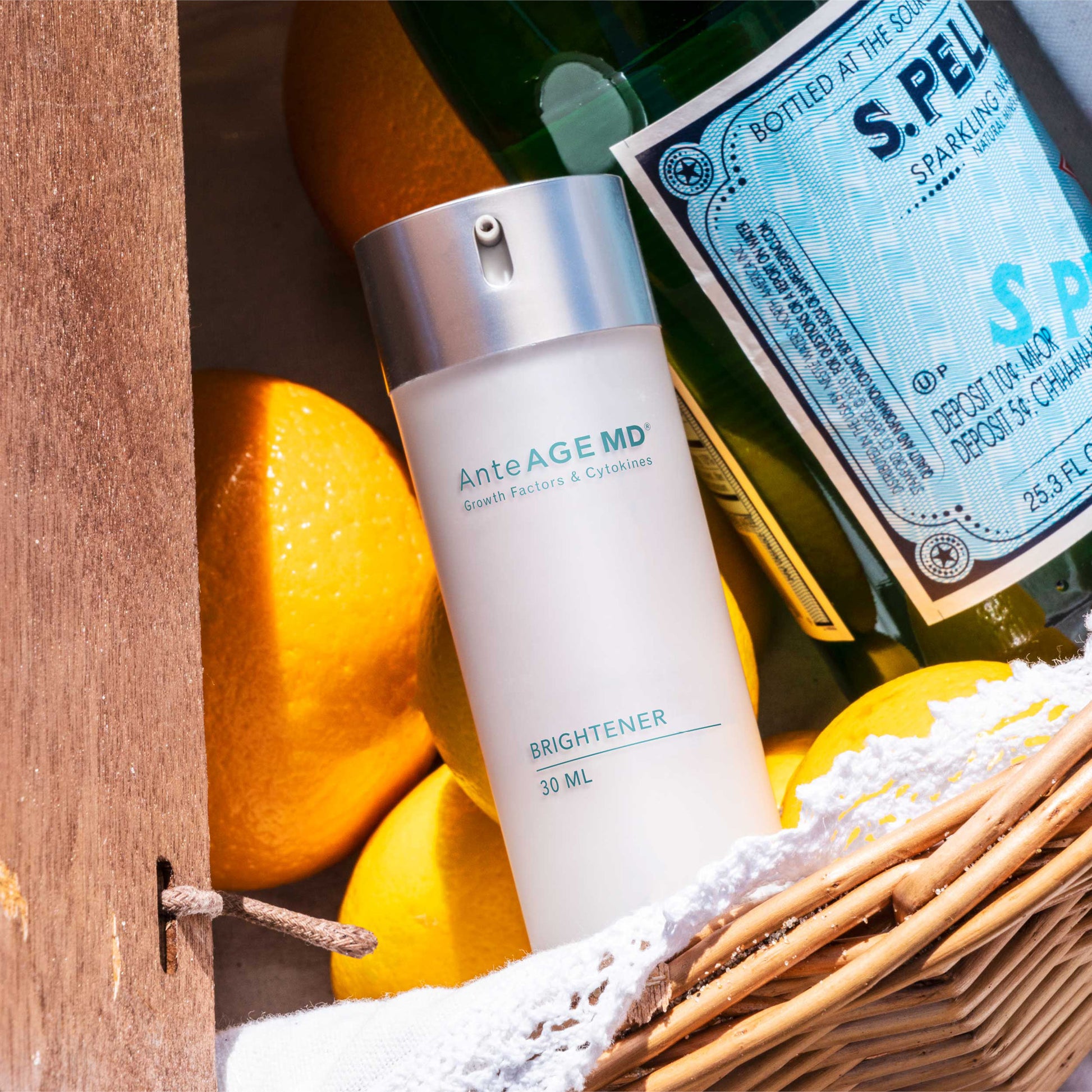 Skincare bottle labeled 'AnteAge MD' with lemons and a bottle of sparkling water on a wooden surface.
