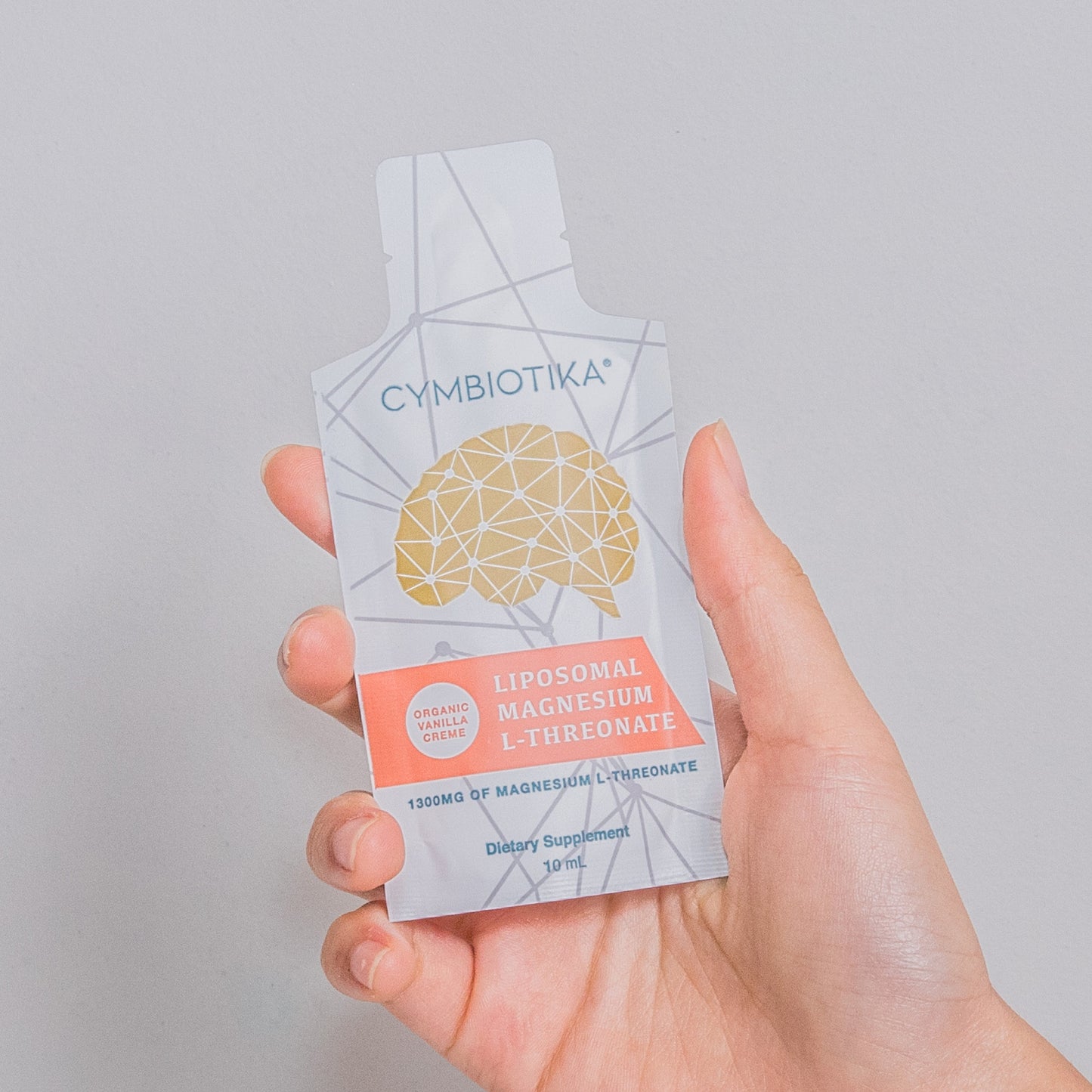 Hand holding a Cymbiotika liposomal magnesium supplement packet against a gray background