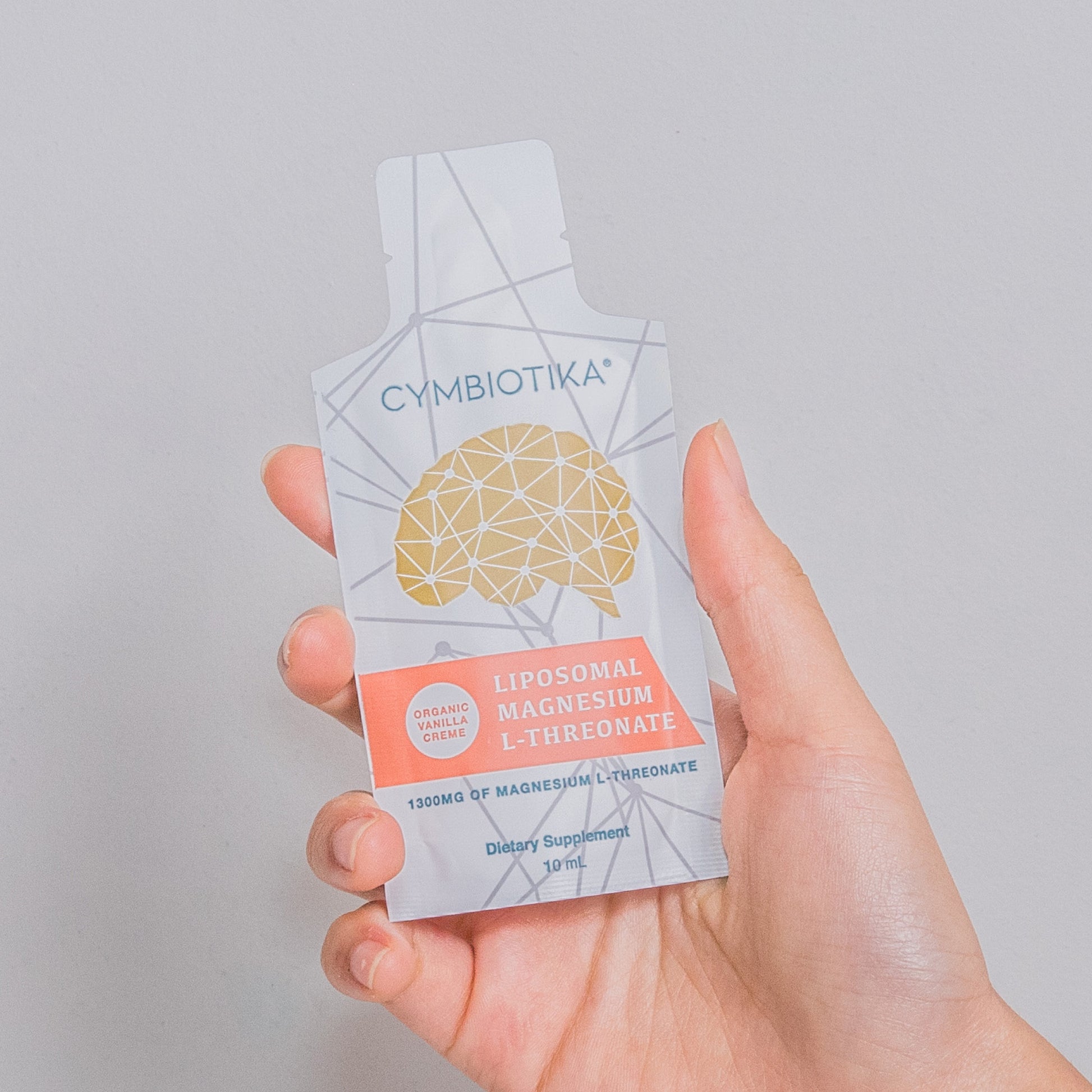 Hand holding a Cymbiotika liposomal magnesium supplement packet against a gray background