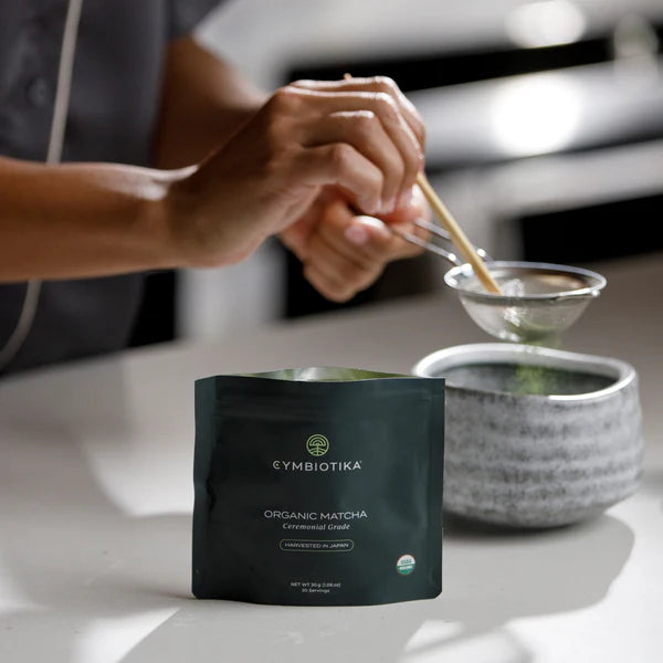 Person making matcha tea with a Cymbiotika organic matcha packet on a table.