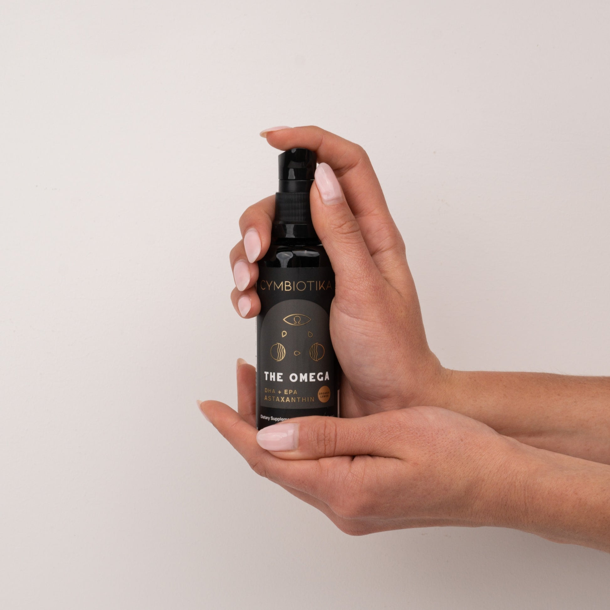 Hand holding a black bottle labeled 'The Omega' against a beige background