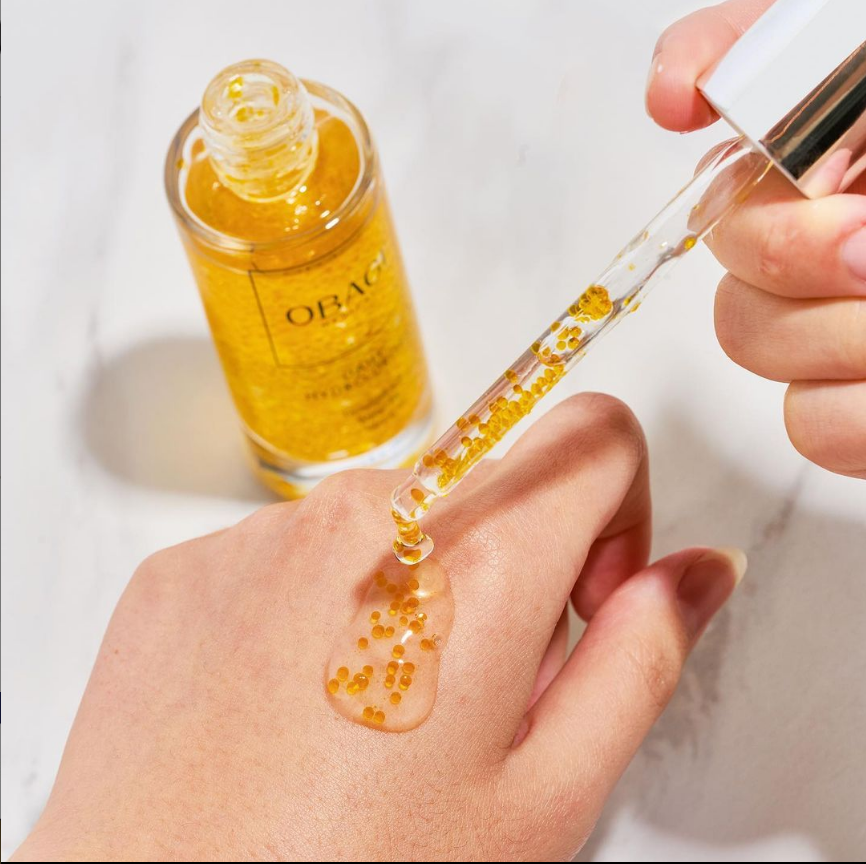 Hand applying OBAC serum to skin with a dropper on a white background