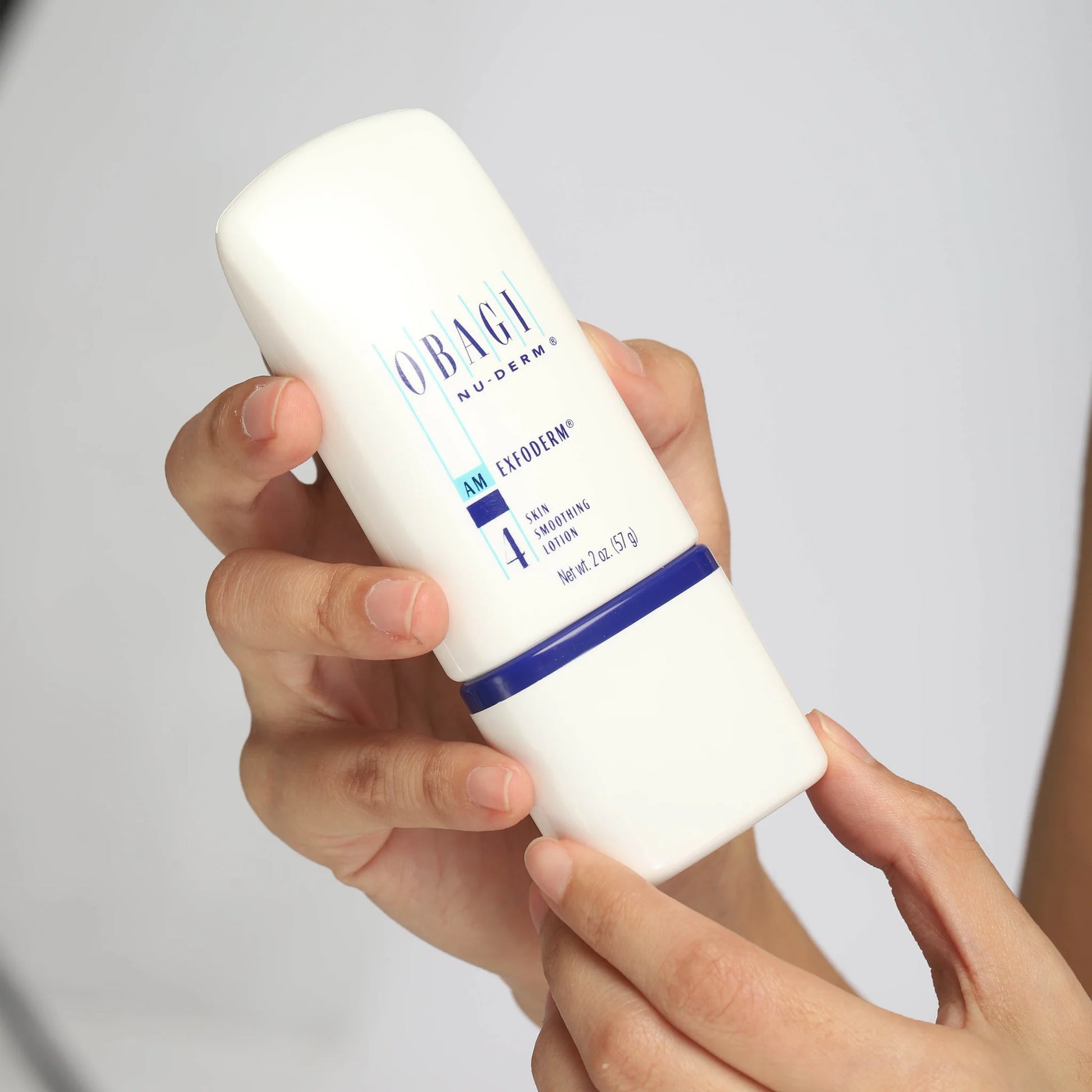 Hand holding a white bottle labeled 'Obagi' against a light gray background