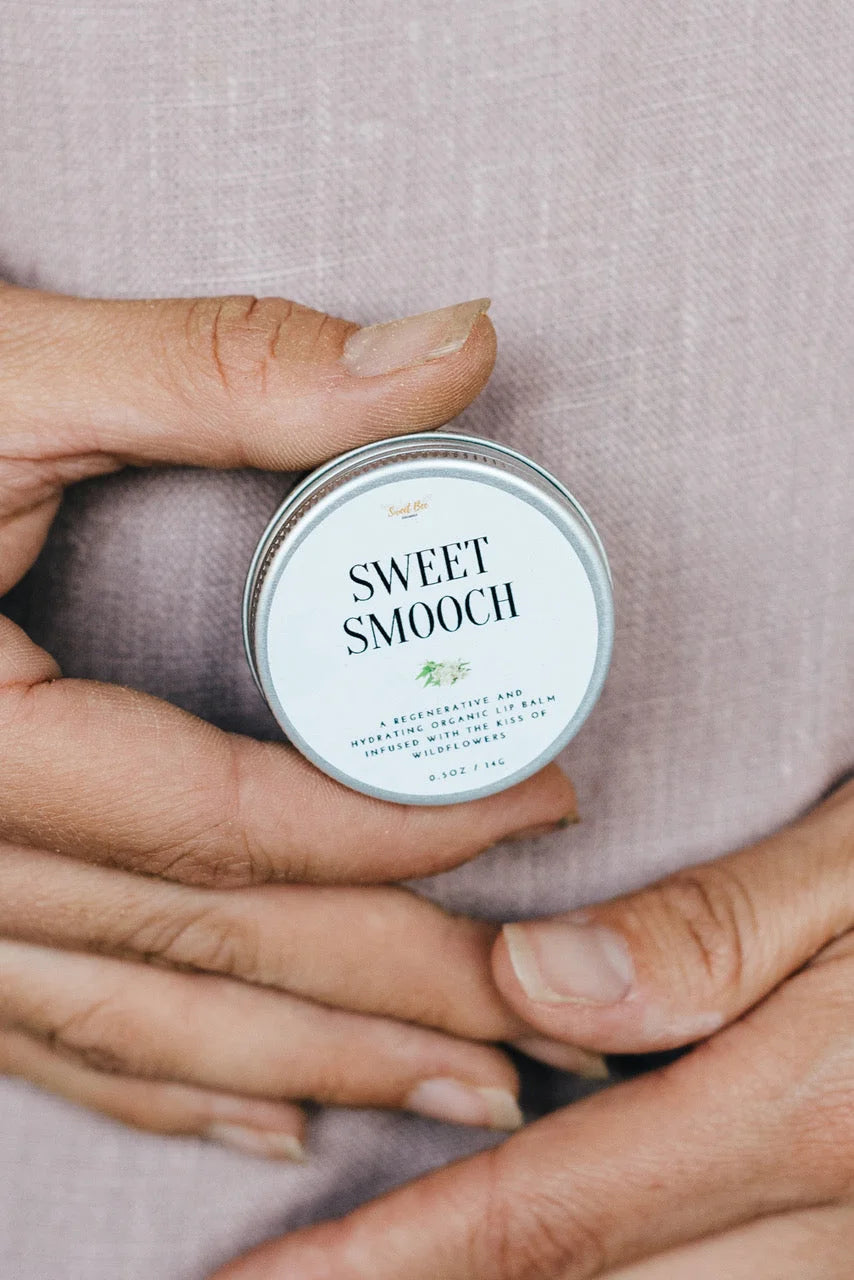 Hand holding a small tin labeled 'Sweet Smooch' against a neutral background