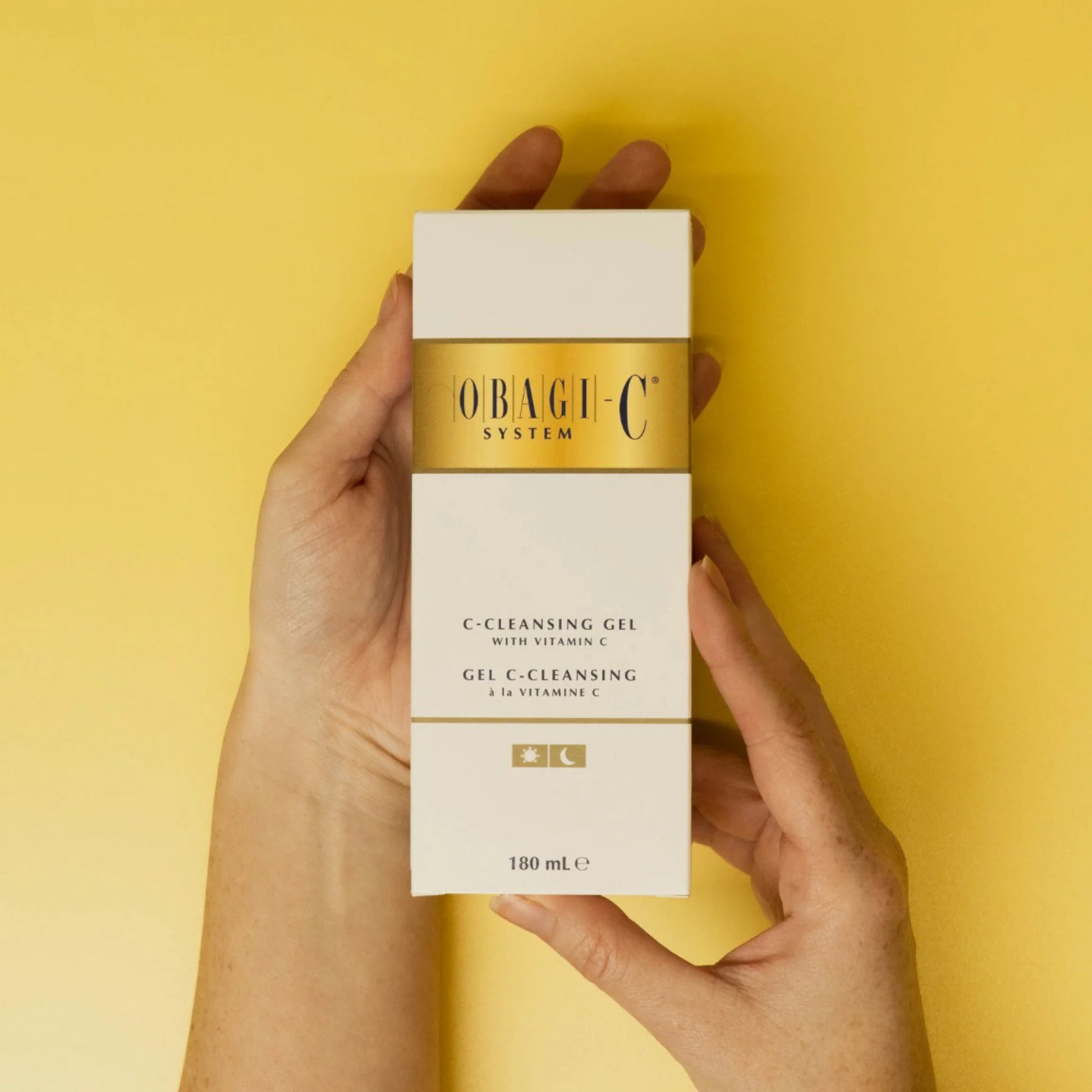 Hand holding a Obagi-C skincare product box against a yellow background