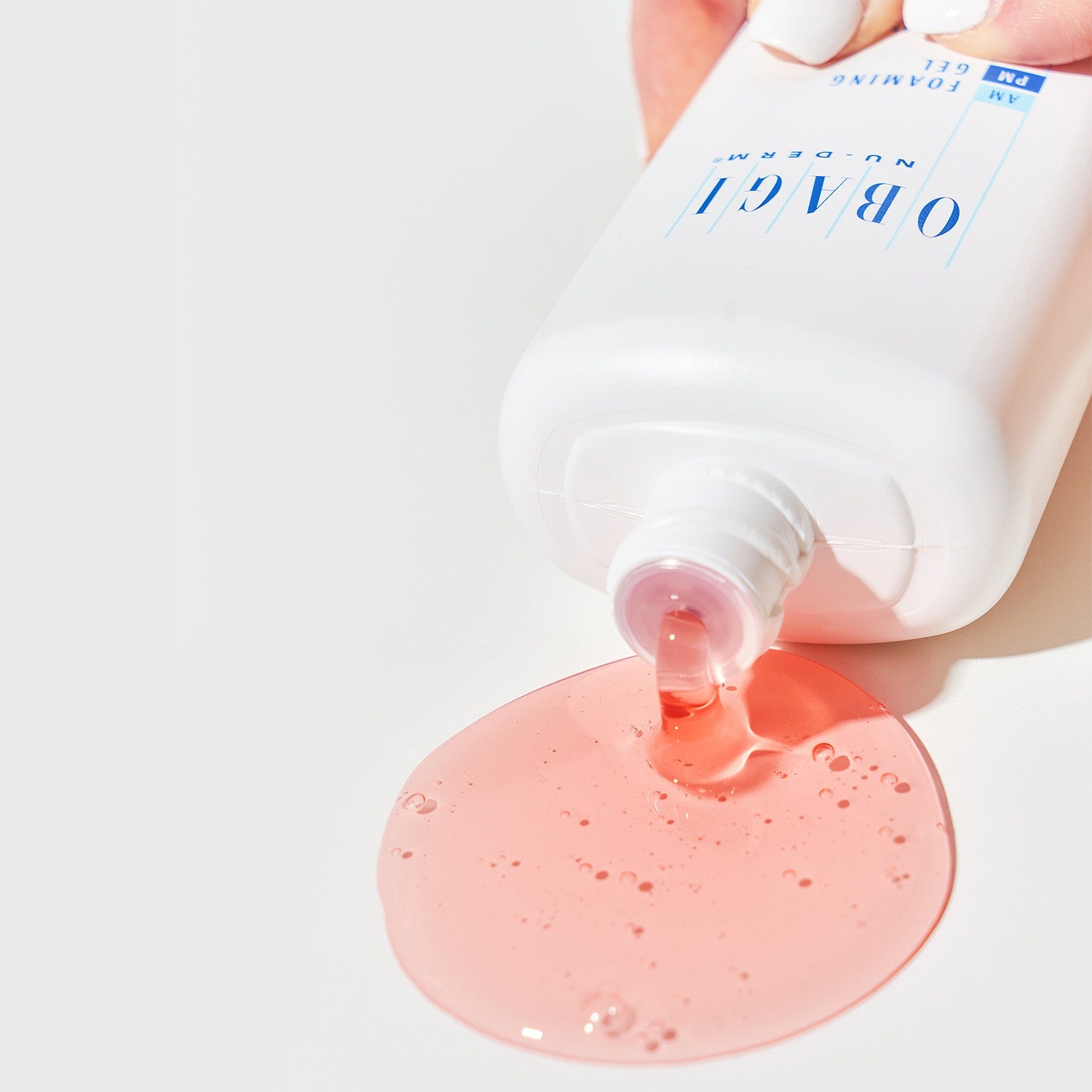 White bottle with pink gel being squeezed onto a white background