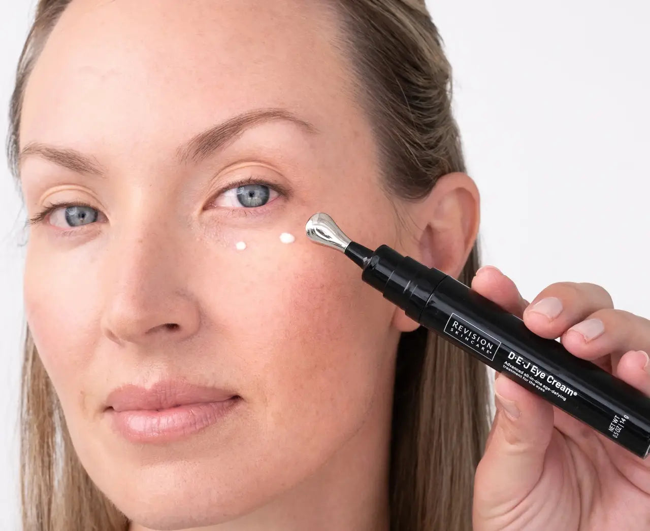Woman applying eye cream with a pen-style applicator on a white background