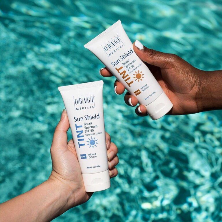 Two hands holding Obagi Sun Shield Sunscreen with a pool background