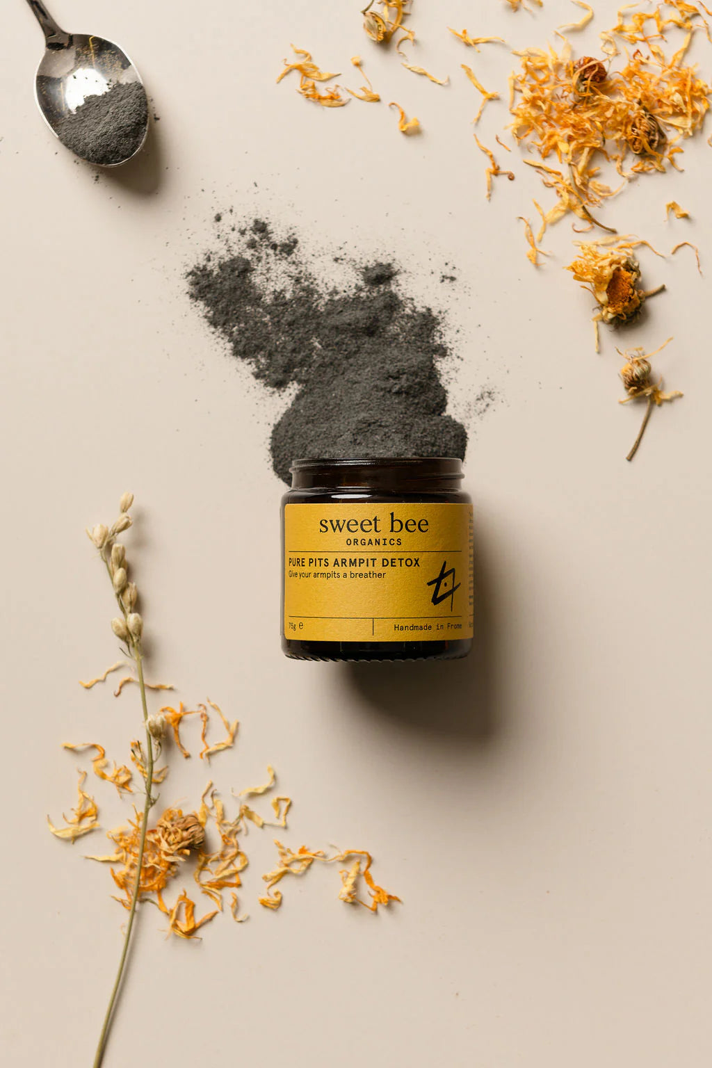 Jar of 'Sweet Bee' product with gray powder and dried flowers on a neutral background