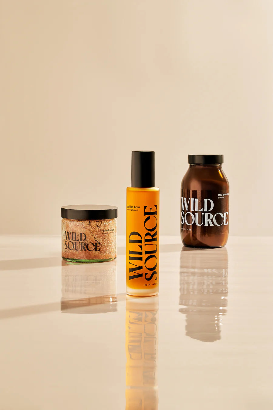 Three 'Wild Source' products on a reflective surface with a beige background