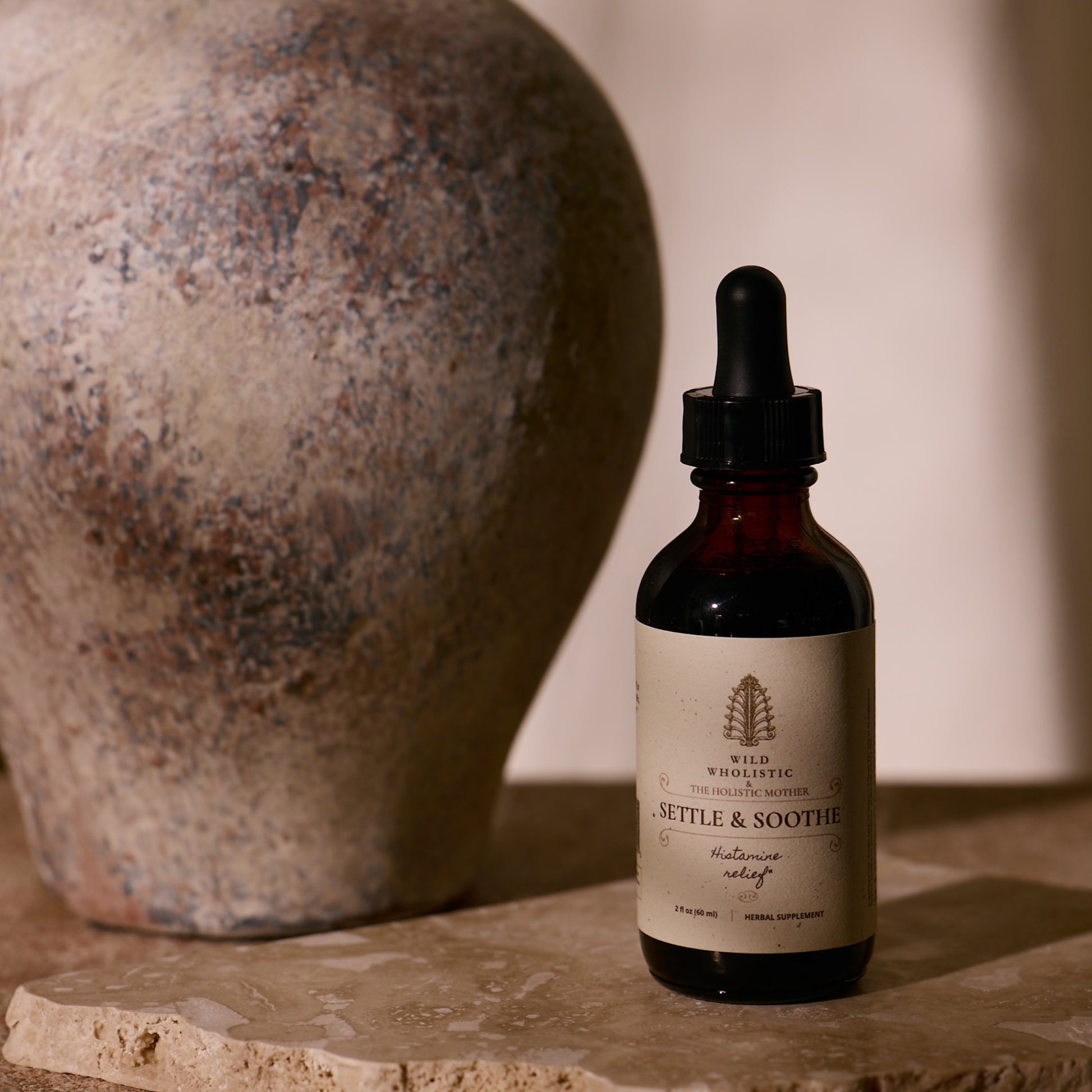 Bottle of 'Settle & Soothe' on a stone surface with a textured vase in the background