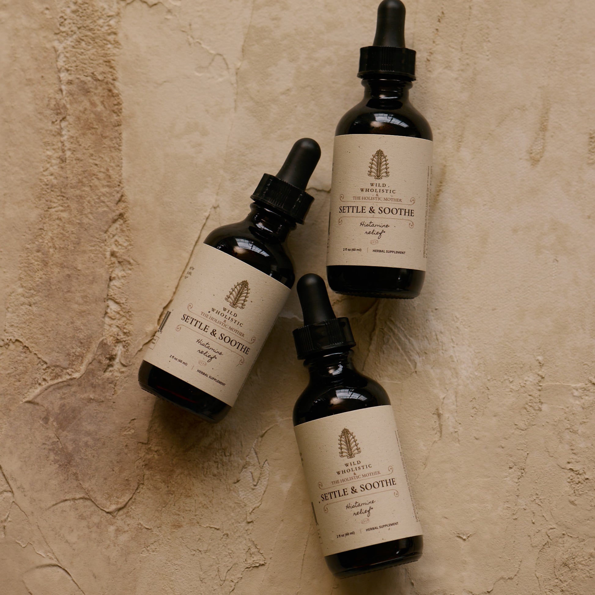 Three bottles of 'Settle & Soothe' on a textured beige surface