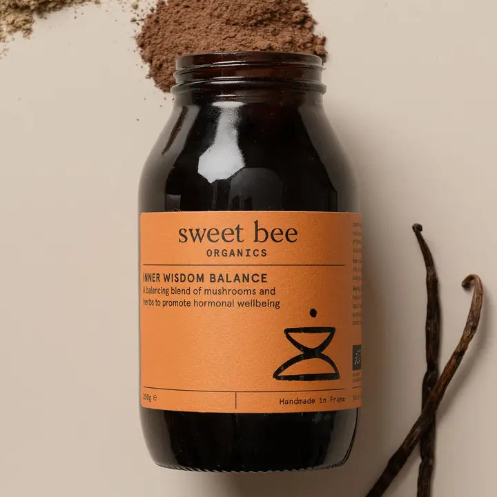 Black jar with 'sweet bee' label on an orange background, surrounded by vanilla beans and cocoa powder.