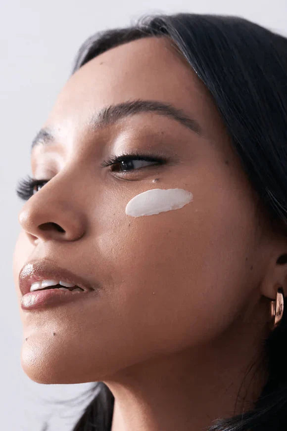 Close-up of a woman's face with a white patch on her cheek against a neutral background