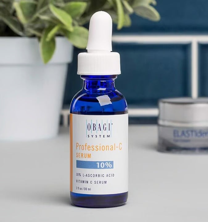 Obagi Professional-G Serum bottle on a surface with a plant and other skincare products in the background.