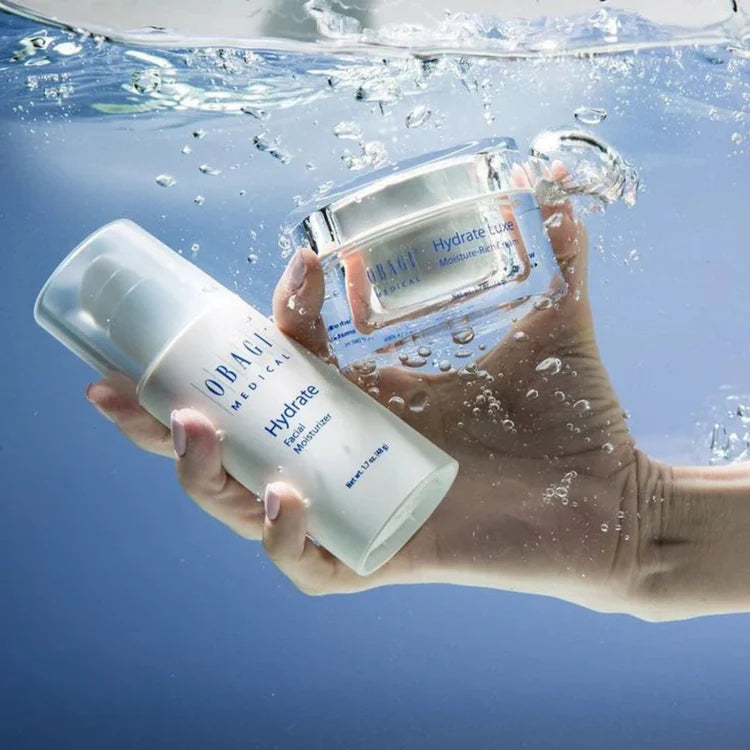 Hand holding OBAGI skincare products underwater with a blue background