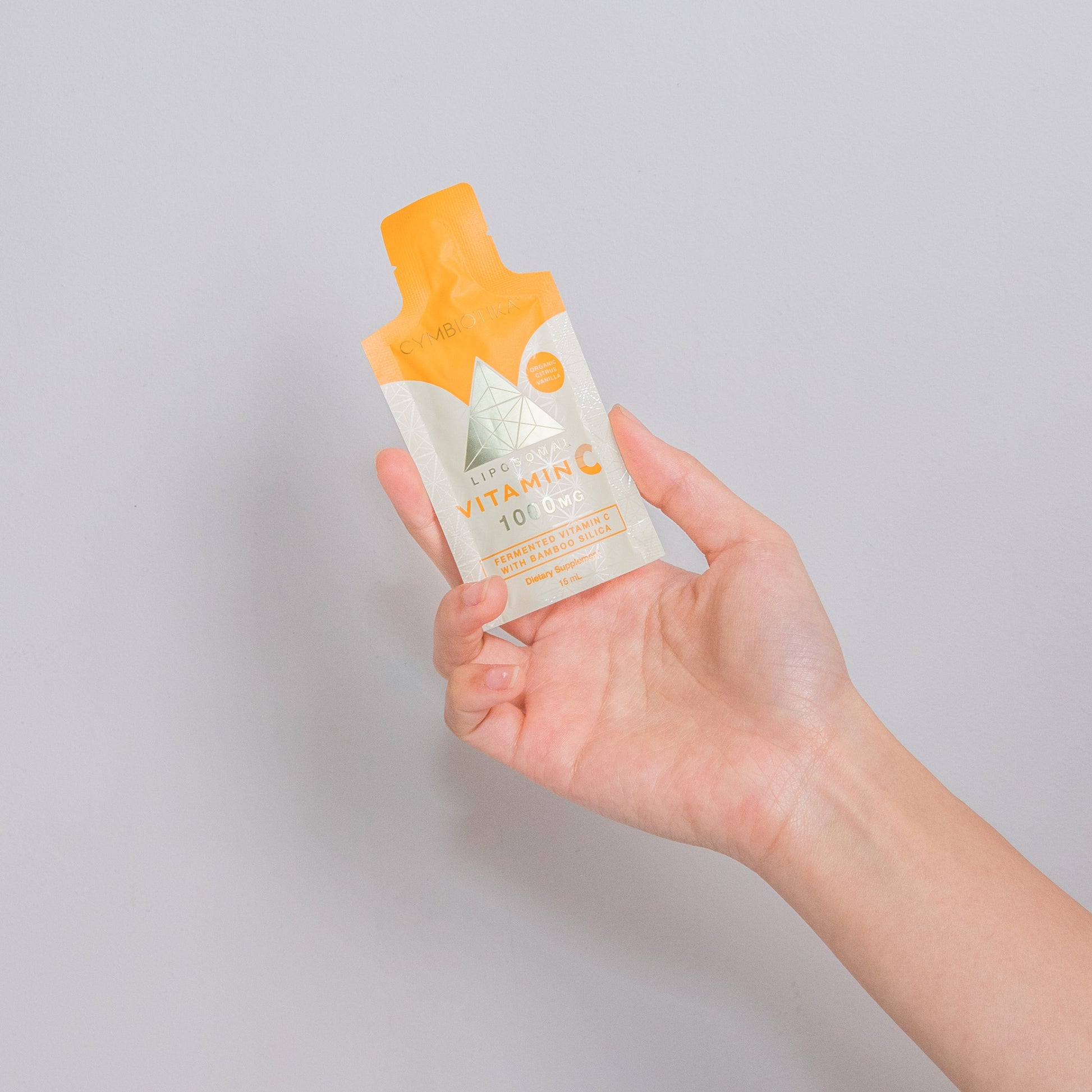 Hand holding a vitamin C product against a gray background